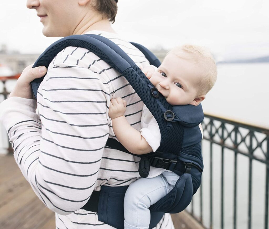 Model carrying baby on her back in the Ergobaby Omni 360 cool mesh in Midnight Blue