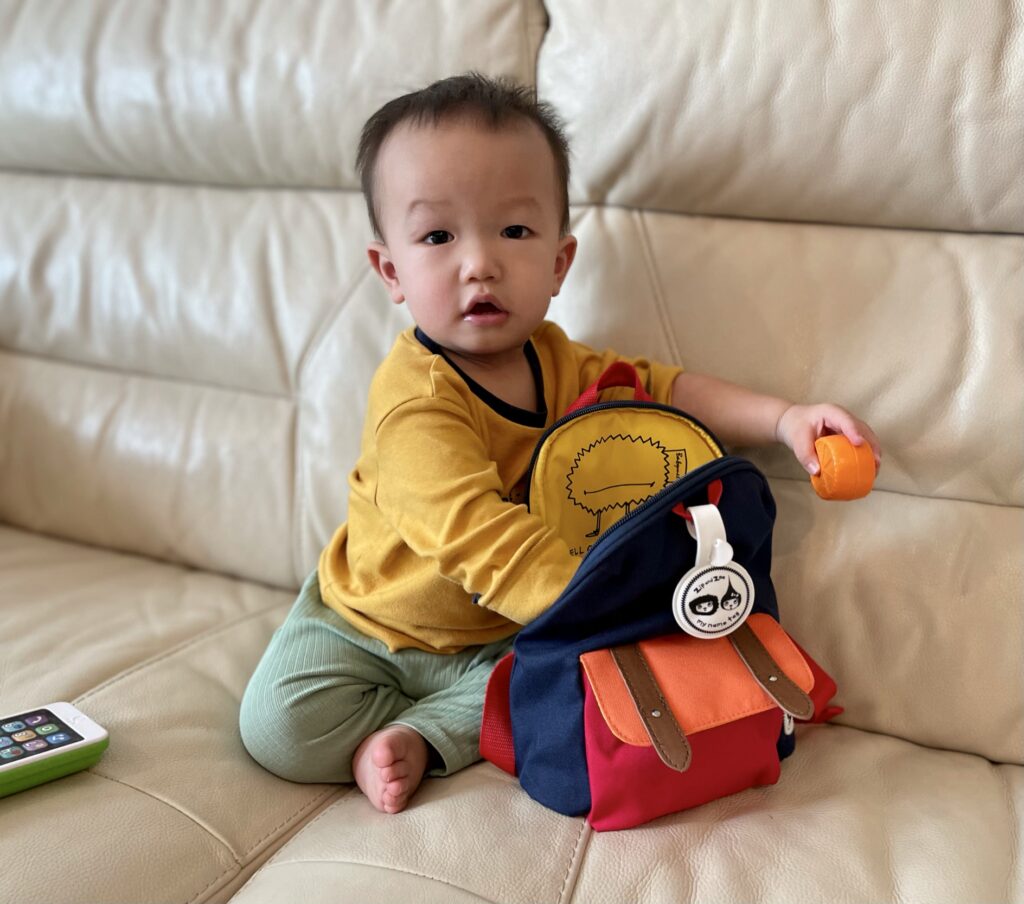 1 year old toddler taking things out of Zip & Zoe mini backpack in navy colourblock