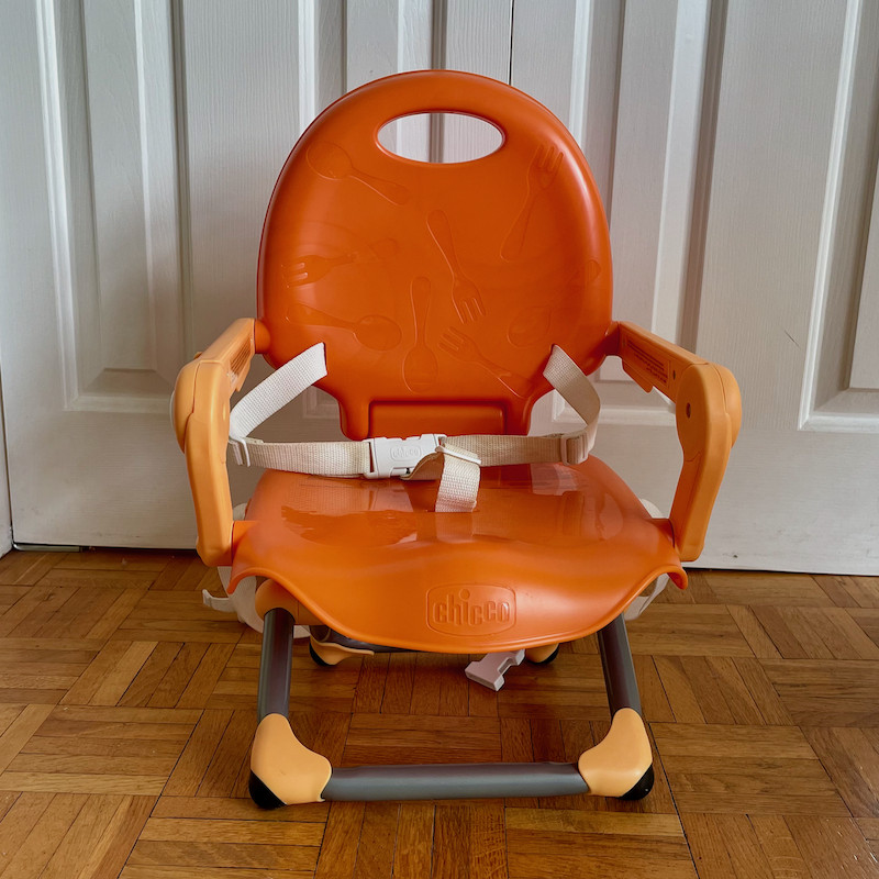 Author's Chicco Pocket Snack Booster Seat in orange with legs folded out front view